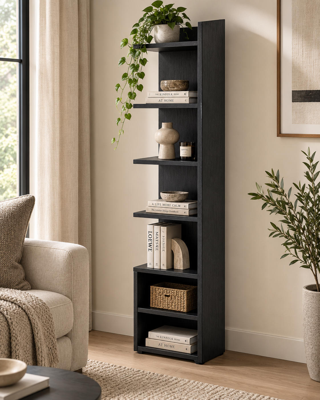 Tall narrow black cypress shelf handcrafted in Kenya, open bays holding books, a trailing plant and a woven basket