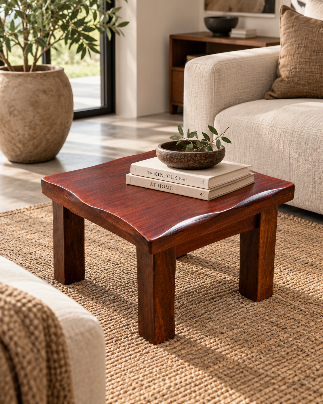 Low square mahogany coffee table from Kenya with a wavy edge and thick legs, holding books and a stone bowl on a jute rug