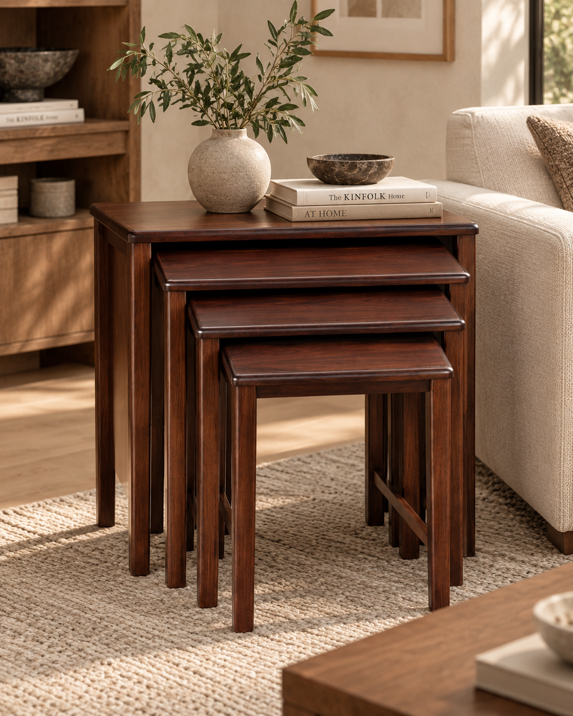 Set of four dark reddish-brown wooden nesting side tables from Kenya, tucked together on a woven rug beside a cream sofa